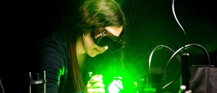 A woman staring into a bright green laser with laser safety goggles